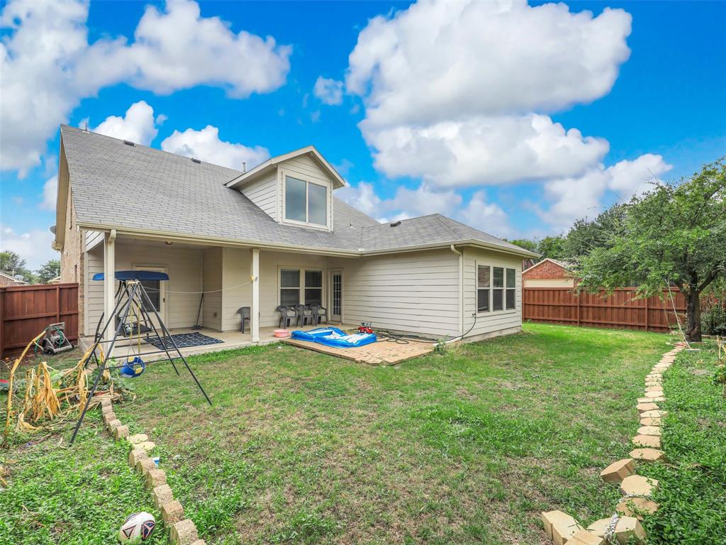 Rear exterior featuring a covered patio, paved stone walkway, and full perimeter wood fencing