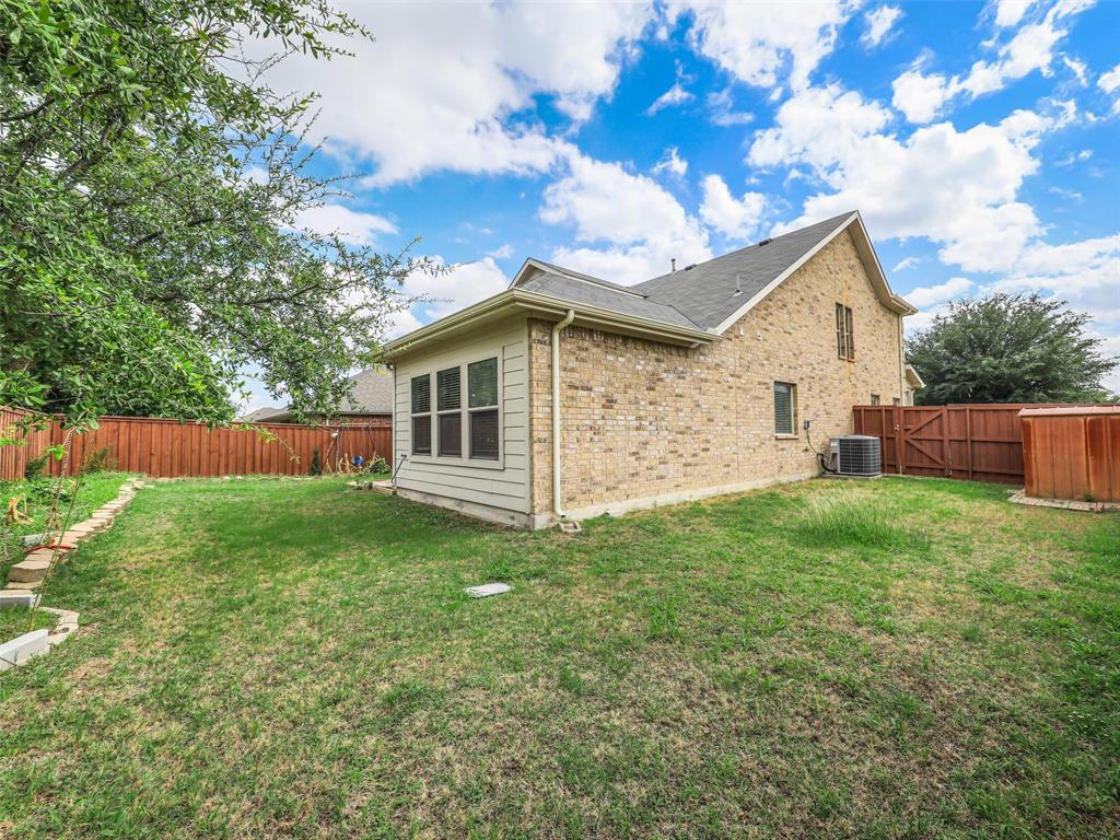 Exterior backyard space featuring a brick and siding facade, wood privacy fencing, and mature trees