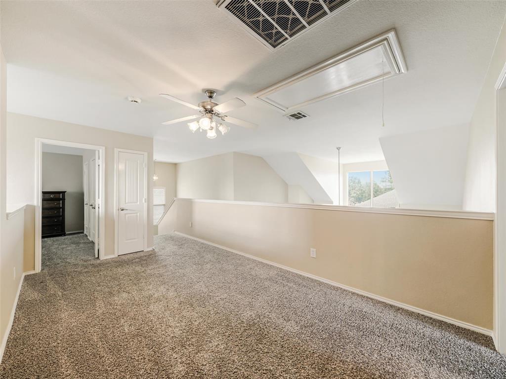 Open area featuring neutral carpet flooring, a ceiling fan with integrated lighting, and an attic access panel