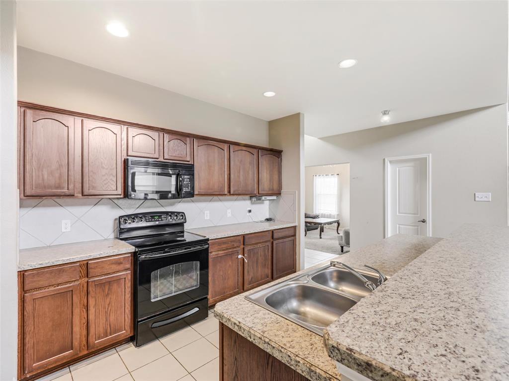 Kitchen featuring wood cabinetry, solid surface countertops, a dual-basin stainless steel sink, tile backsplash, and built-in black appliances