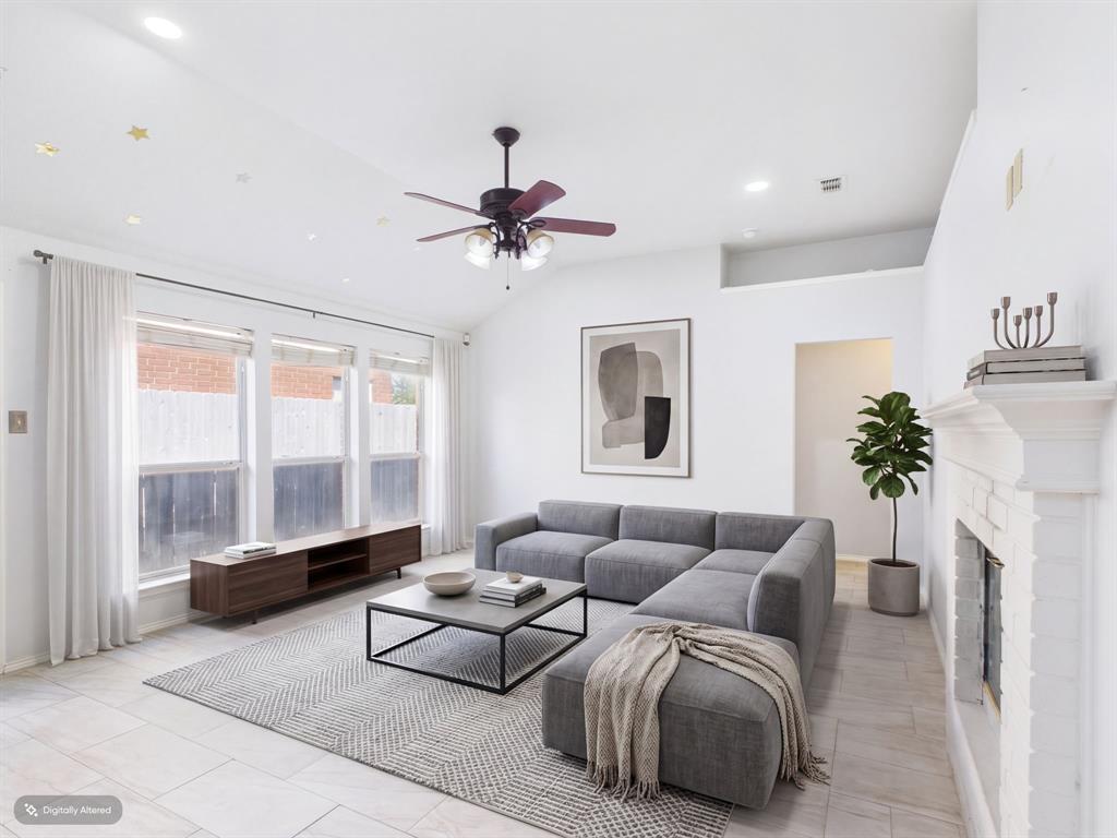 Vaulted ceiling with a central multi-blade ceiling fan, expansive windows, light-toned tile flooring, and a painted brick fireplace with a mantel