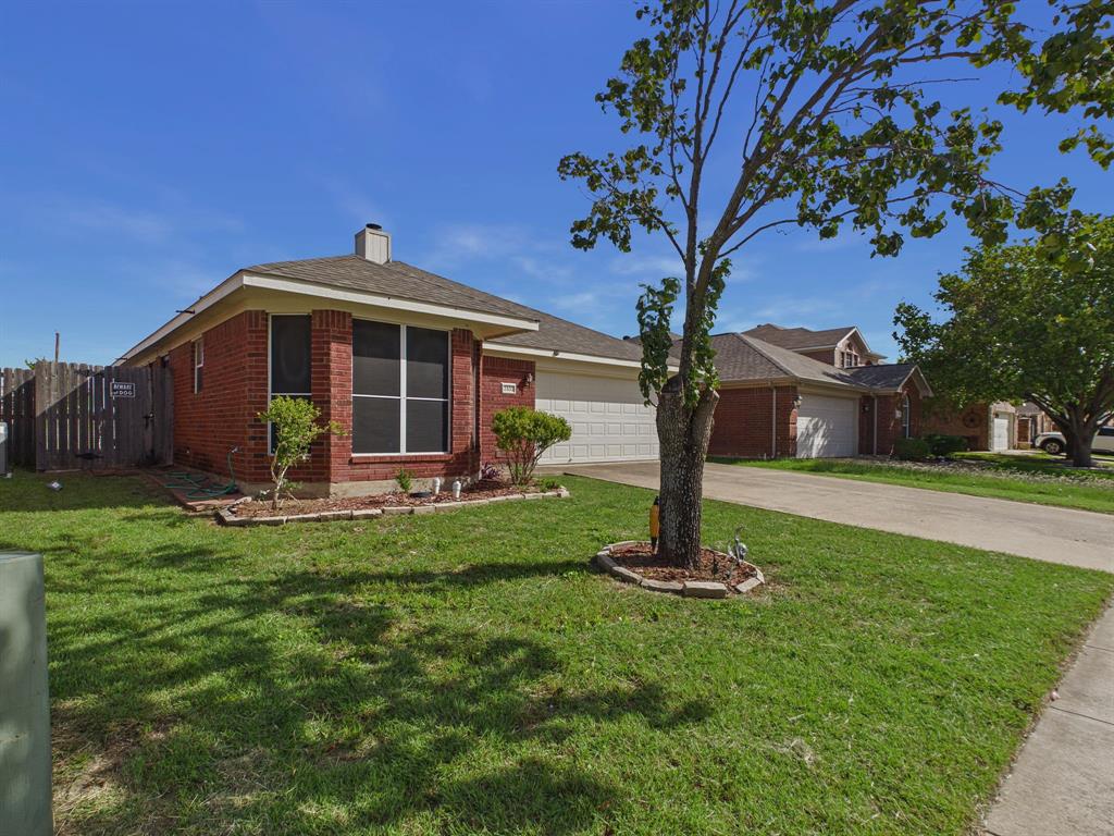 Single-story brick exterior featuring a multi-hipped shingle roof, attached two-car garage, and a fenced side yard