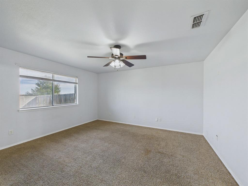 Neutral-toned interior room featuring wall-to-wall carpeting, a large sliding window, and a ceiling fan with integrated lighting