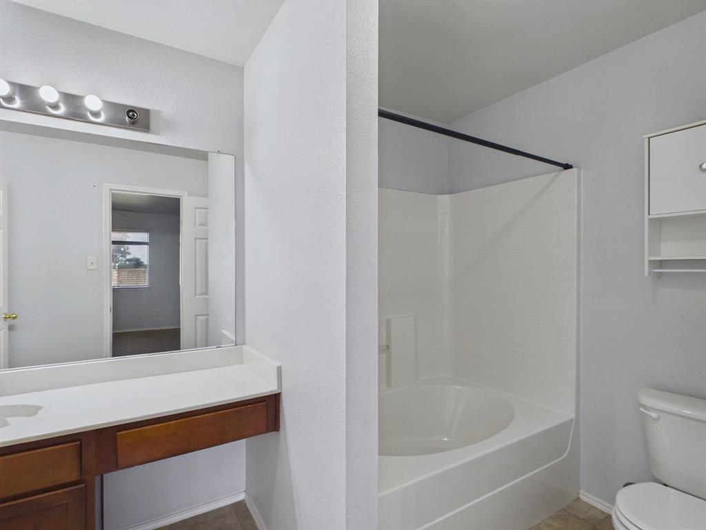 Bathroom featuring a white vanity with a rectangular sink, wall-mounted light fixture, full-width mirror, and a built-in tub-shower combination with a matte black shower rod