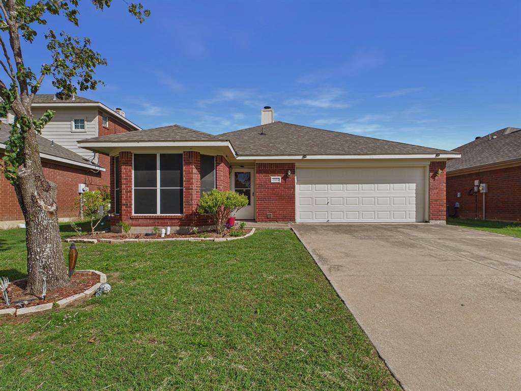 Single-story residence featuring a brick exterior, shingled roof, attached two-car garage, concrete driveway, and a front garden bed with stone edging