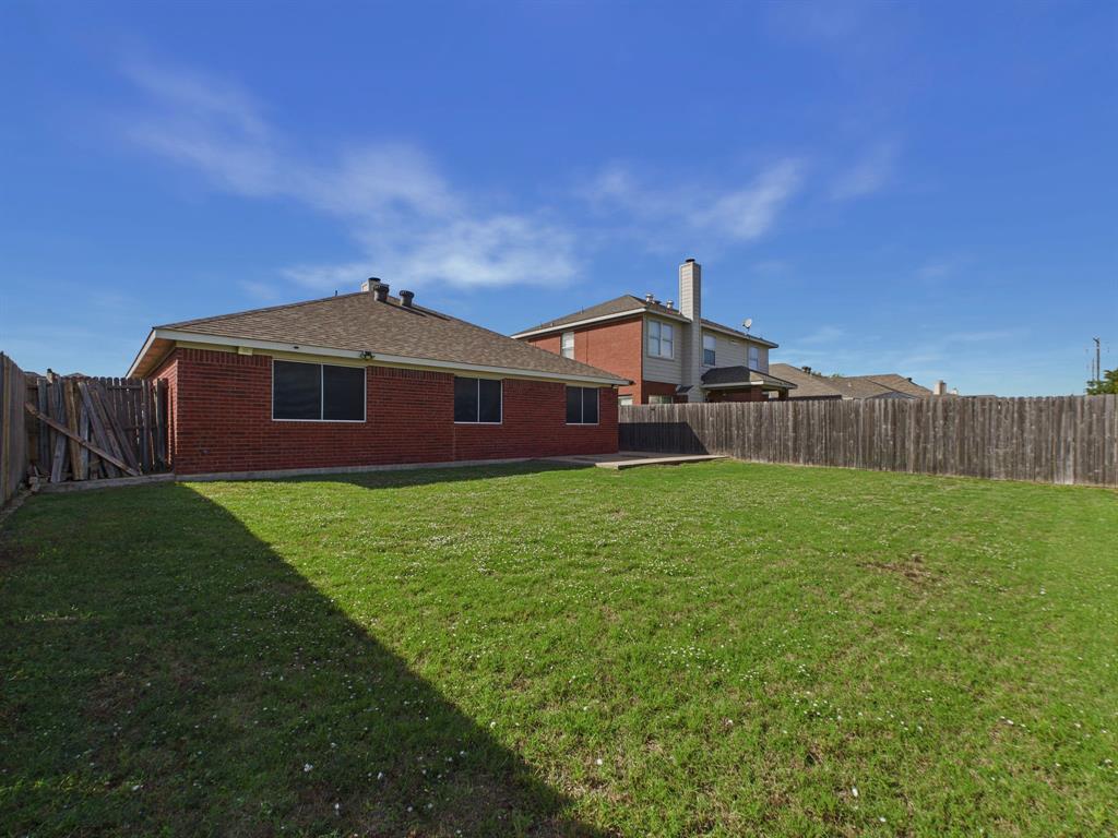 Rear exterior featuring a brick facade, hip roof with composition shingles, concrete patio, and fenced-in backyard with a grass lawn
