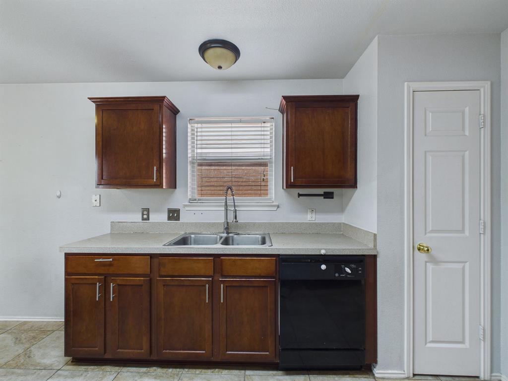 Kitchen featuring stained wood cabinetry, solid surface countertops, dual-basin stainless steel sink with high-arc faucet, and black dishwasher