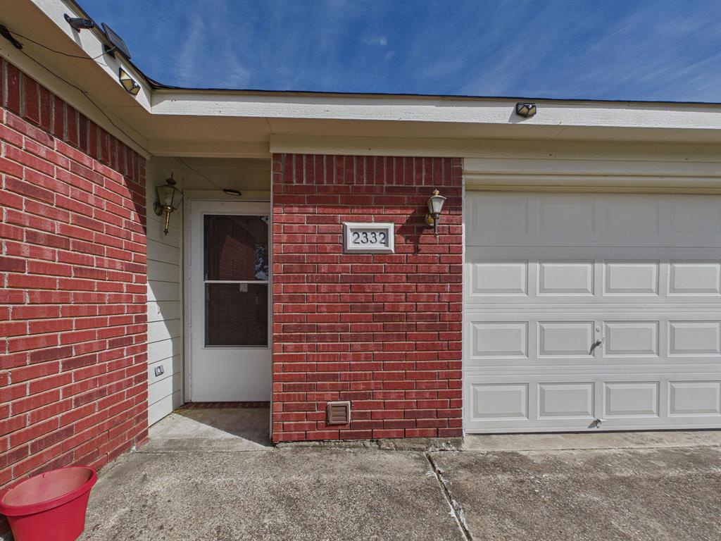 Red brick facade with a white, paneled garage door, recessed entryway, and exterior wall-mounted lighting