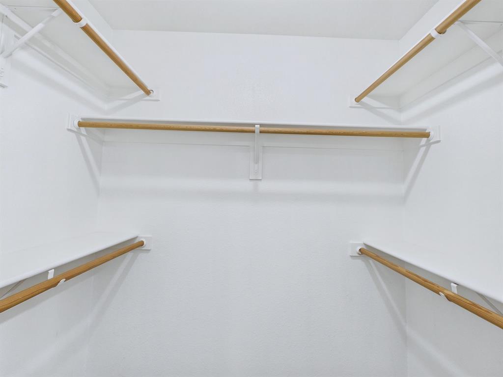 Walk-in storage space featuring multi-level white shelving and integrated natural wood-finish hanging rods