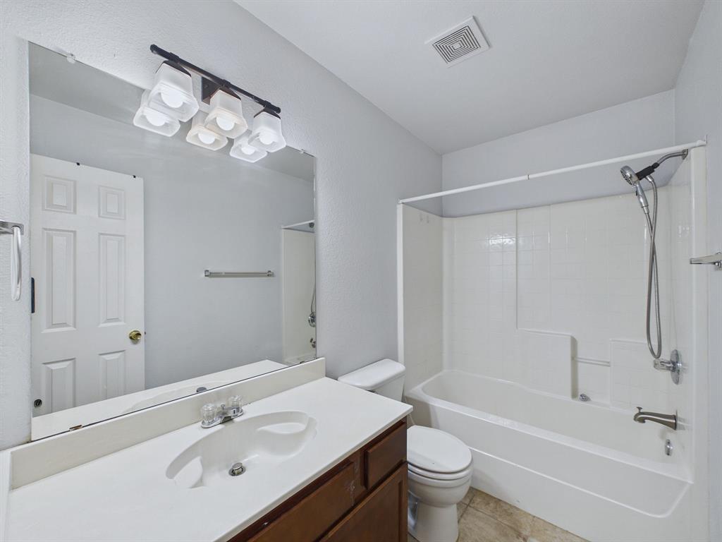 Full-width vanity with white solid-surface countertop and integrated sink, chrome multi-light fixture, oversized frameless mirror, and shower-tub combination with a handheld showerhead