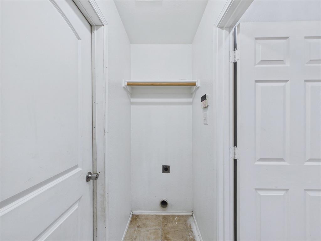Utility alcove featuring tile flooring, a wall-mounted shelf with a rod, and dedicated appliance hookups