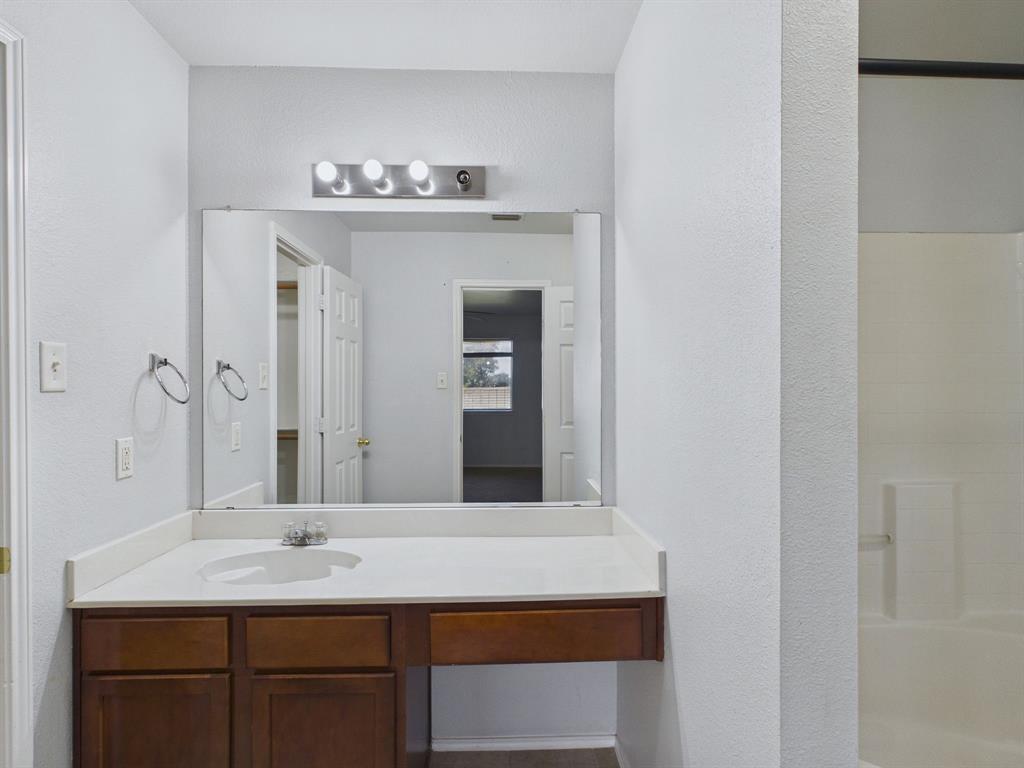 Bathroom featuring a wood-finish vanity with a seamless integrated sink, solid surface countertop, large wall-mounted mirror, and a three-bulb vanity light fixture