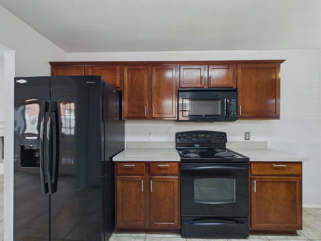 Kitchen featuring wood cabinetry, solid-surface countertops, and a suite of black appliances including a built-in microwave, electric range, and refrigerator