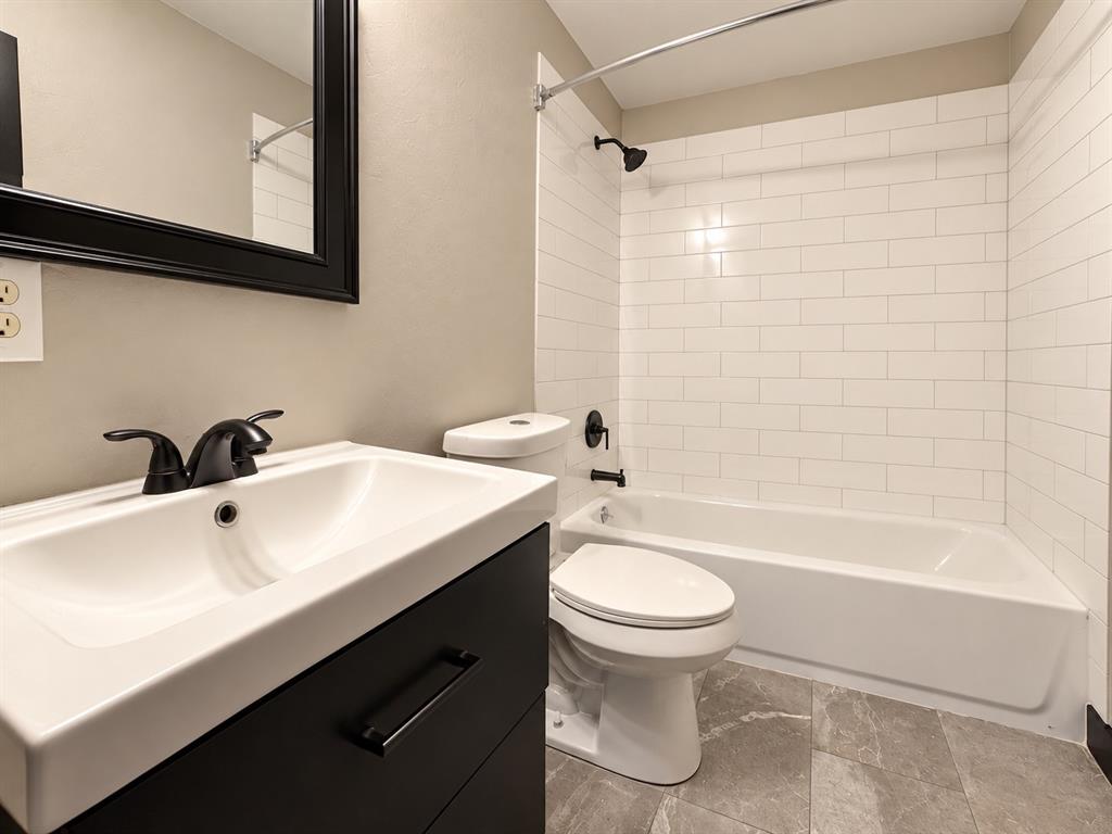 Updated bathroom featuring a modern vanity, subway tile tub surround, and coordinating dark fixtures.