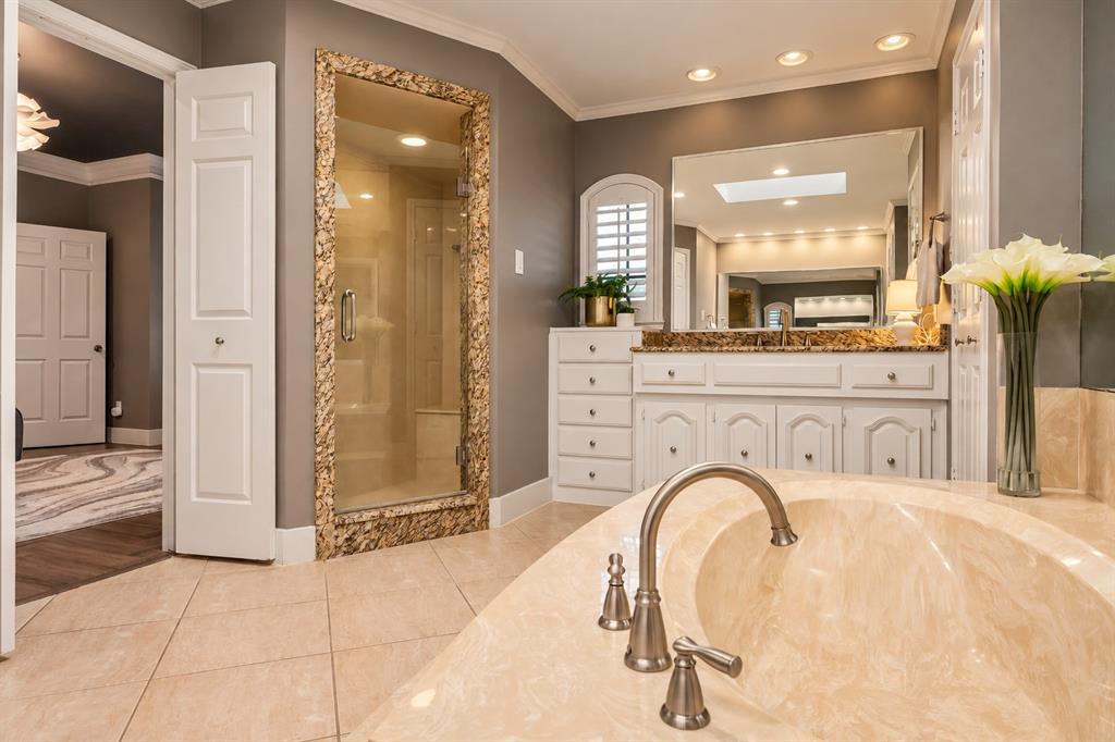 Bathroom featuring an oval soaking tub with a stone-finish deck, a custom-tiled walk-in shower with a stone surround, white cabinetry, a large wall-mounted mirror, and tile flooring