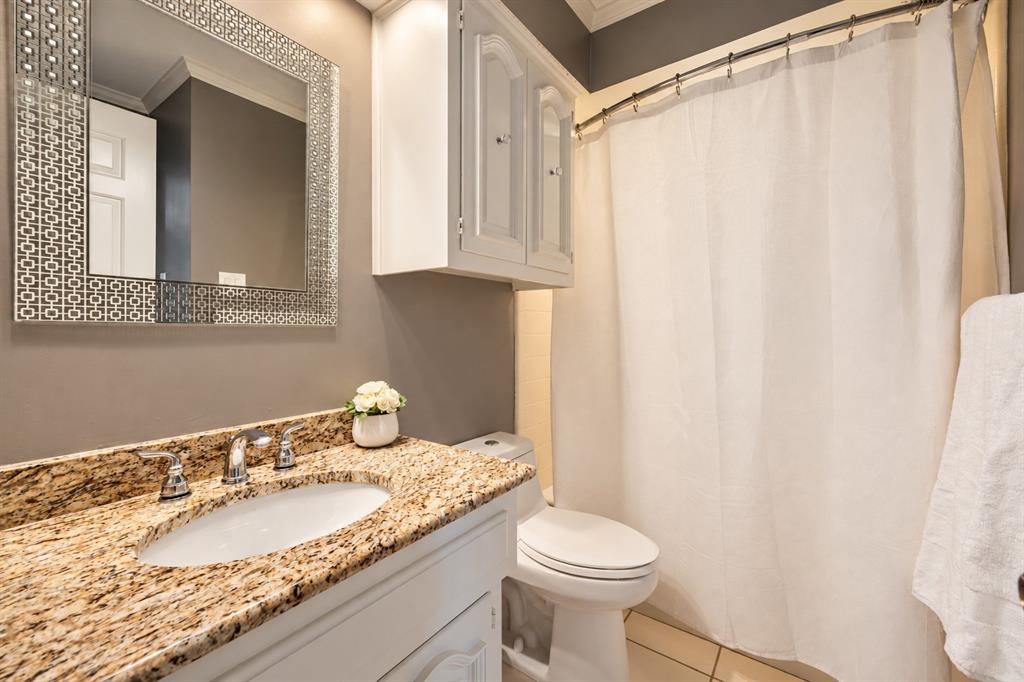 Bathroom featuring a stone-surface countertop, white cabinetry with upper storage, undermount sink with dual-handle faucet, and patterned decorative mirror