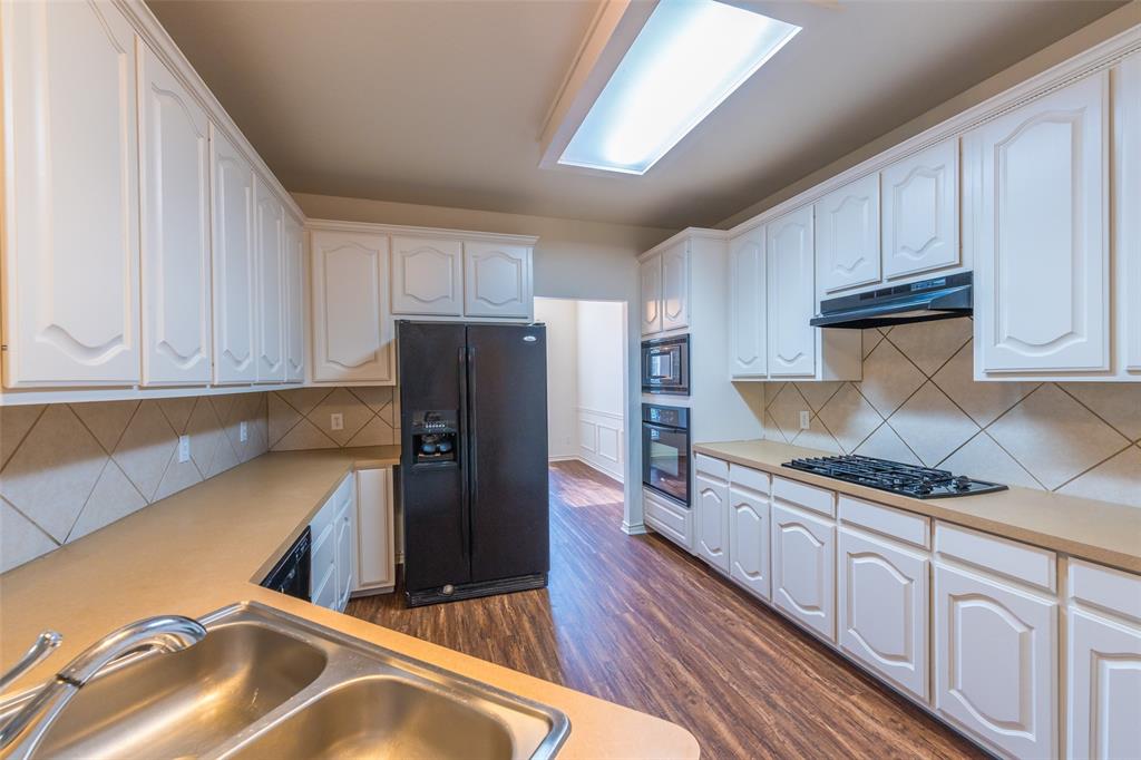 Kitchen featuring white cabinetry, wood-finish flooring, diamond-pattern tile backsplash, dual-basin stainless steel sink, and built-in appliances