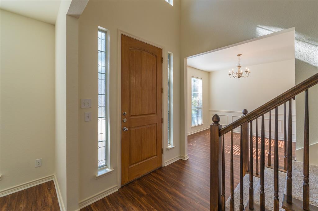 Foyer featuring wood-finish flooring, a solid wood door with decorative glass sidelights, and a staircase with a stained wood handrail and balusters