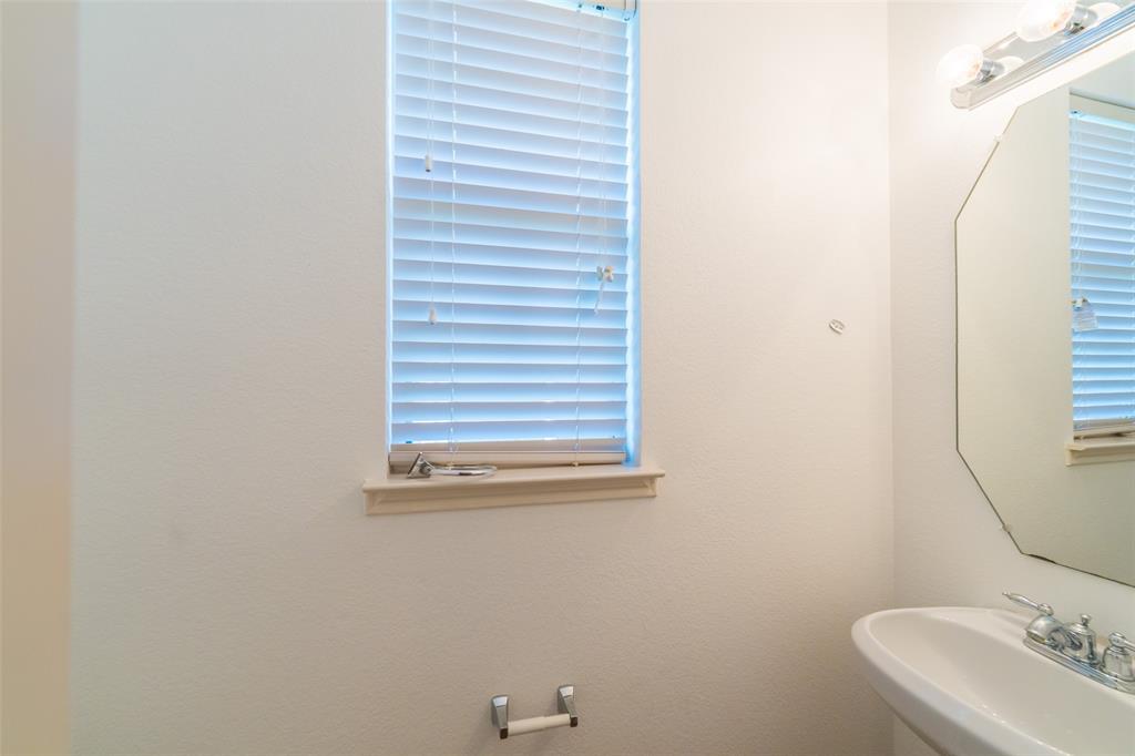 Octagonal wall-mounted mirror, pedestal sink with chrome faucet, window with integrated blinds, and chrome hardware fixtures
