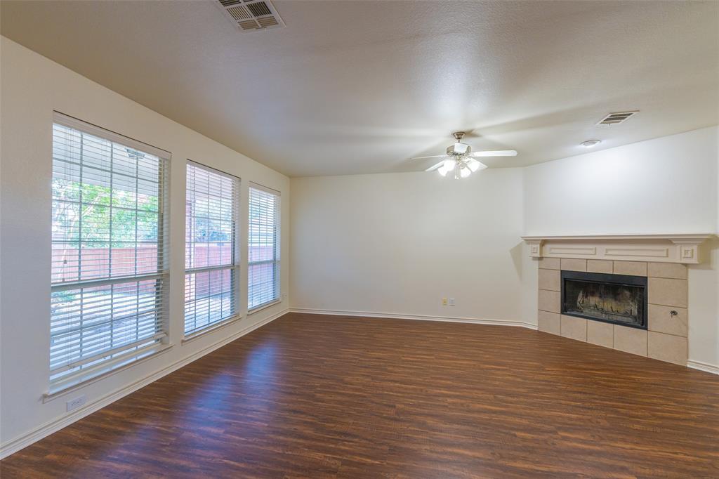 Living area featuring wood-finish flooring, a corner fireplace with a decorative mantel and stone-finish surround, triple pane windows, and a ceiling-mounted light fixture