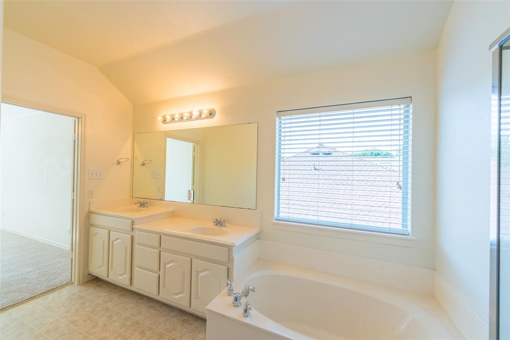Bathroom featuring a dual-sink vanity with white cabinetry, a large wall-mounted vanity mirror, a soaking tub with deck-mounted chrome fixtures, and a window with horizontal blinds