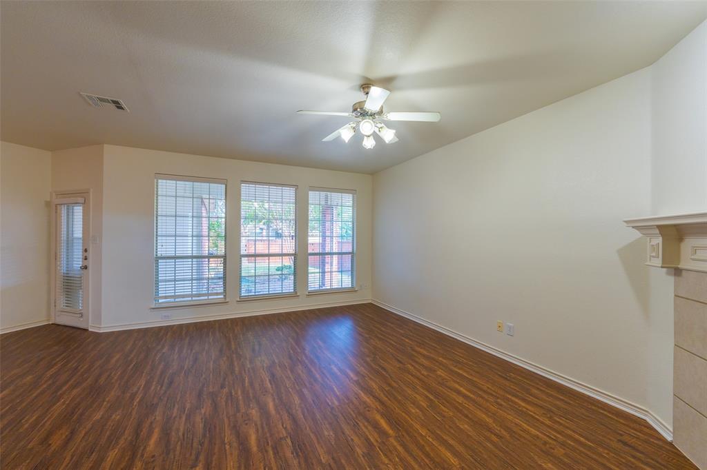Living area featuring wood-finish flooring, a ceiling fan with integrated lighting, a fireplace with a decorative mantel, and grid-pattern windows