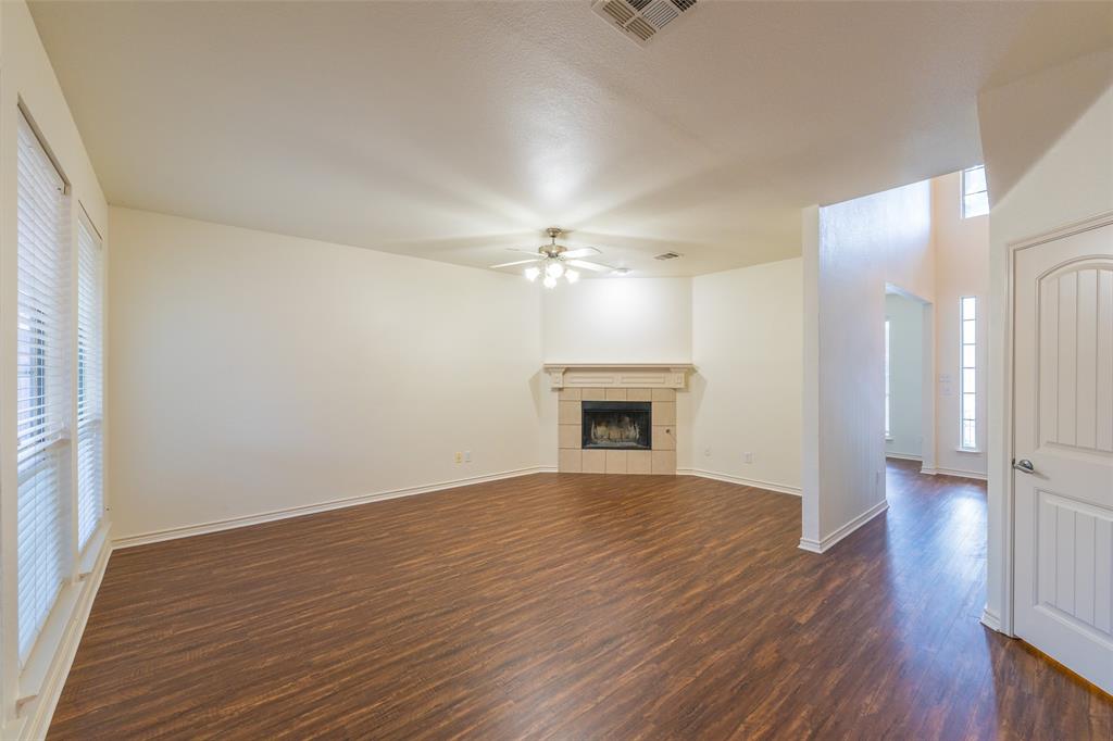 Living area featuring wood-finish flooring, a corner fireplace with a decorative mantel, ceiling fan with light fixture, and vertical windows with blinds