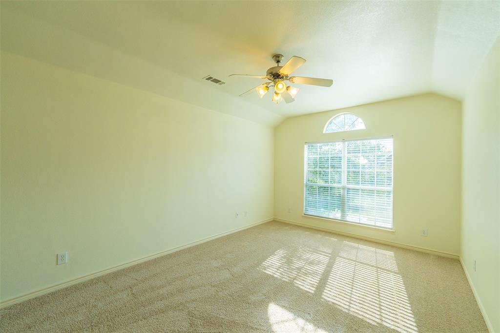 Vaulted ceiling featuring a central multi-blade ceiling fan with integrated lighting, neutral carpeted flooring, and a large window topped with an arched transom