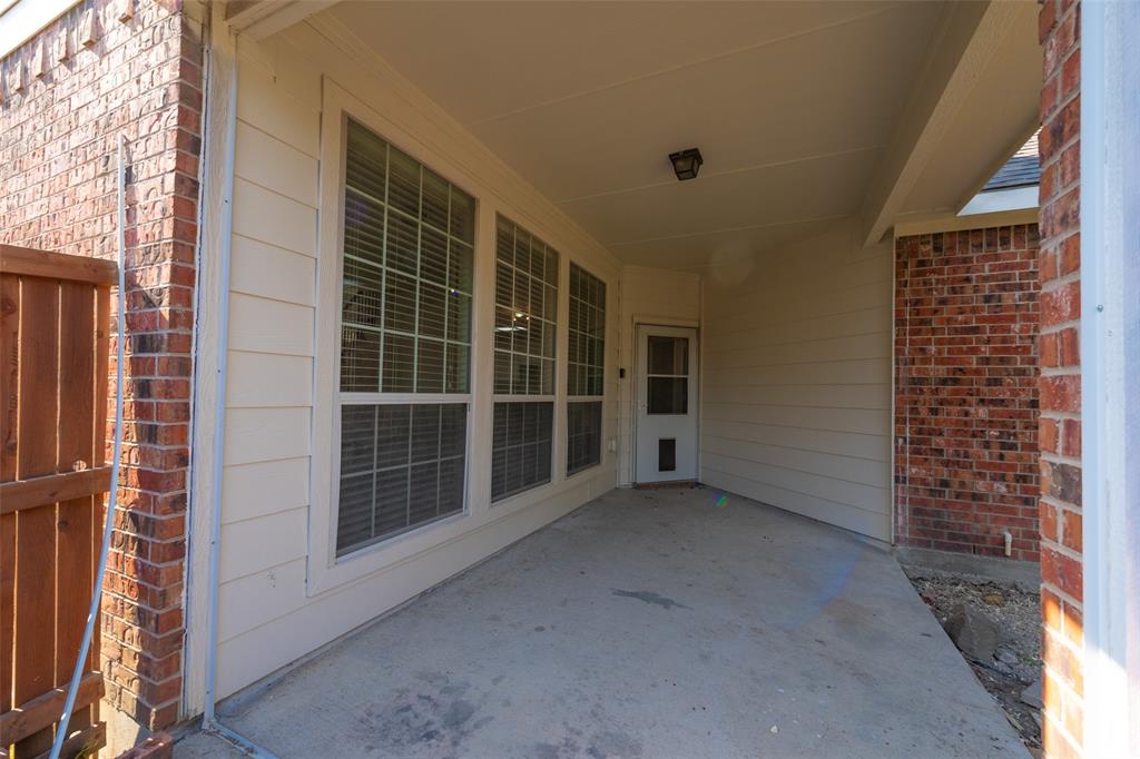 Covered concrete patio featuring a brick and horizontal siding exterior, expansive multi-pane windows, and a flush-mount ceiling light fixture