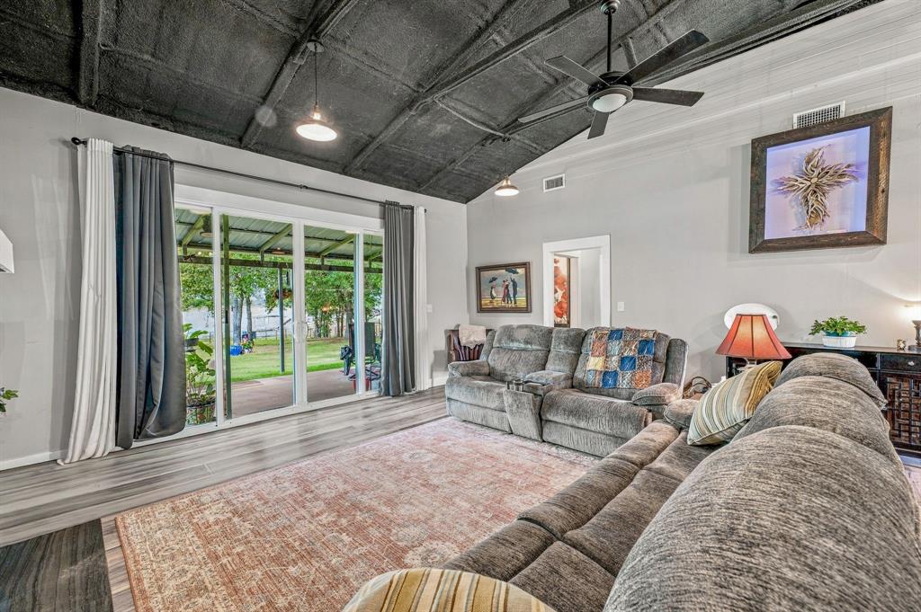 Vaulted ceiling with dark finish, wood-finish flooring, sliding glass doors, and ceiling fan with integrated lighting