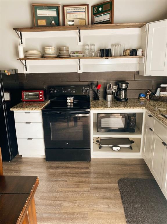 Kitchen featuring white cabinetry, stone-finish countertops, dark horizontal tile backsplash, wood-finish flooring, and dual open wooden wall-mounted shelves