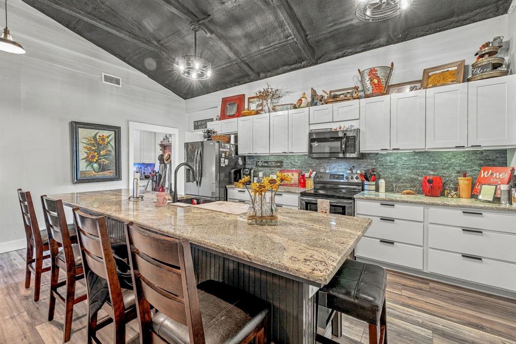 Kitchen featuring white Shaker-style cabinetry, a large granite-topped island with an integrated sink, vaulted ceilings, and wood-finish vinyl flooring