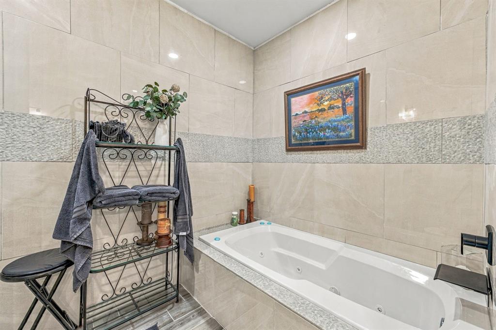 Soaking tub with integrated jetted system, large-format neutral wall tiling, decorative mosaic tile inlay, and wall-mounted matte black faucet