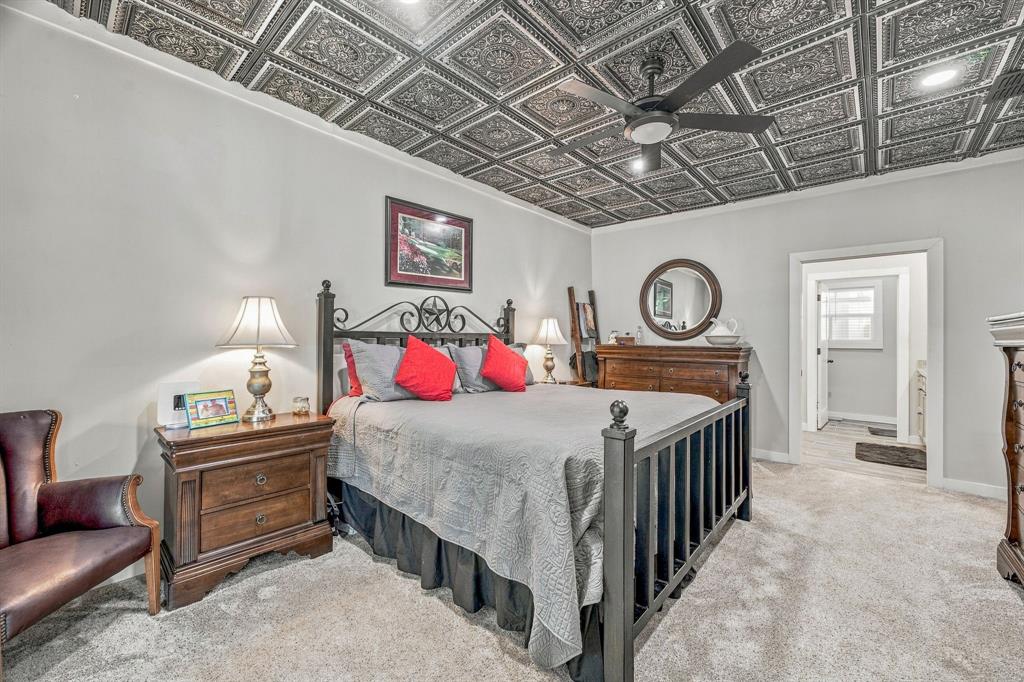 Decorative coffered ceiling with intricate tin-style tiles, matte black ceiling fan, and neutral wall-to-wall carpeting