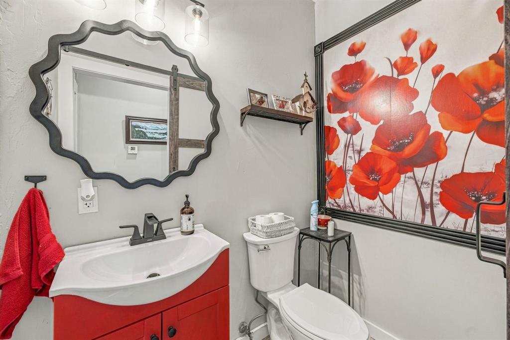Half Bath off Living area for quests with vanity featuring a curved sink basin and matte black faucet, scalloped wall mirror, and three-light overhead fixture