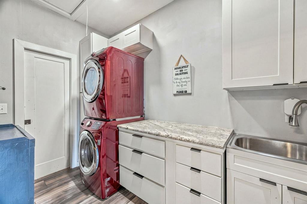 White Shaker-style cabinetry featuring matte black hardware, stone-finish countertops, stainless steel drop-in sink, high-arc faucet, and wood-finish flooring.  Stacked washer/dyer negotiable.