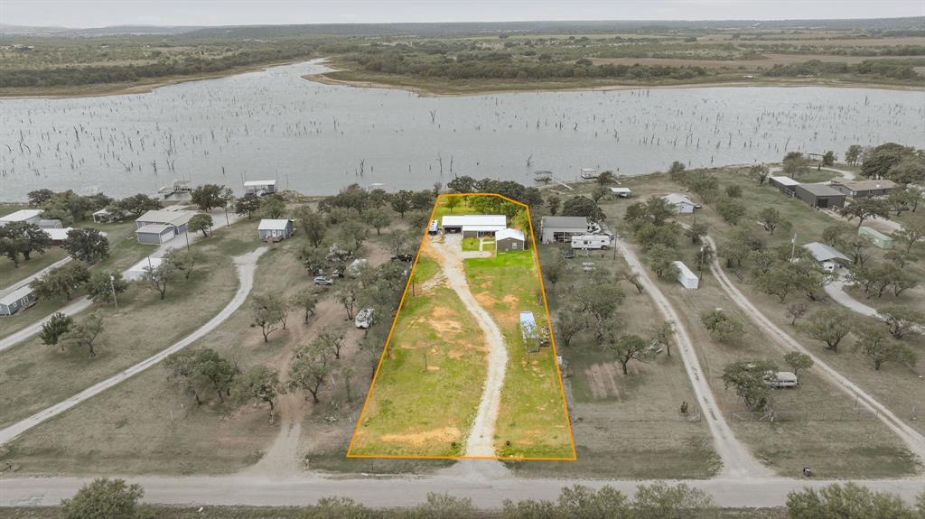 Aerial perspective of a waterfront property featuring a long private driveway, open acreage, and mature trees