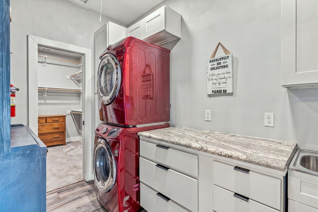 Utility room connects to the walk-in bedroom closet features granite-surface countertops, custom shaker-style cabinetry, overhead storage units, and an integrated stainless steel sink