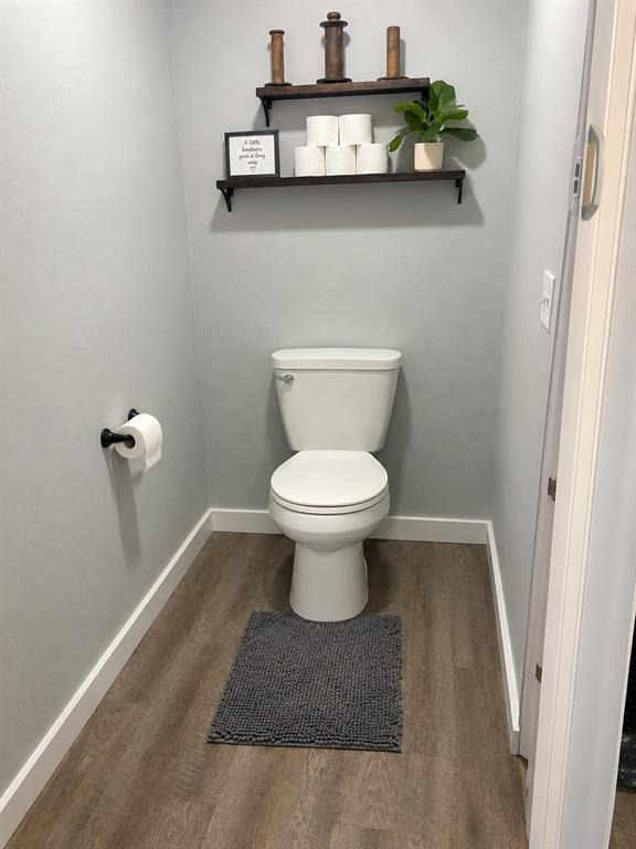 Water closet featuring wood-finish flooring, a two-piece toilet, and a matte black toilet paper holder