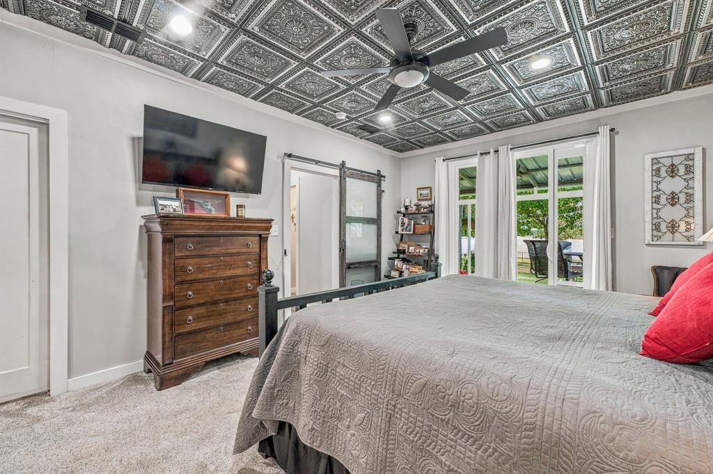 Detailed decorative ceiling tile, matte black ceiling fan with integrated lighting, sliding barn door with frosted glass panel, and floor-to-ceiling glass sliding door with exterior access