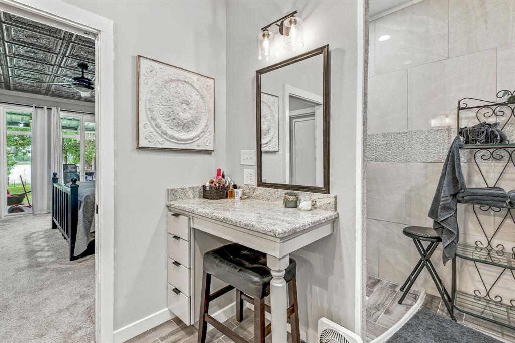 Built-in vanity with stone countertop, multi-drawer cabinetry, framed wall mirror, dual-bulb vanity lighting, and tiled walk-in shower
