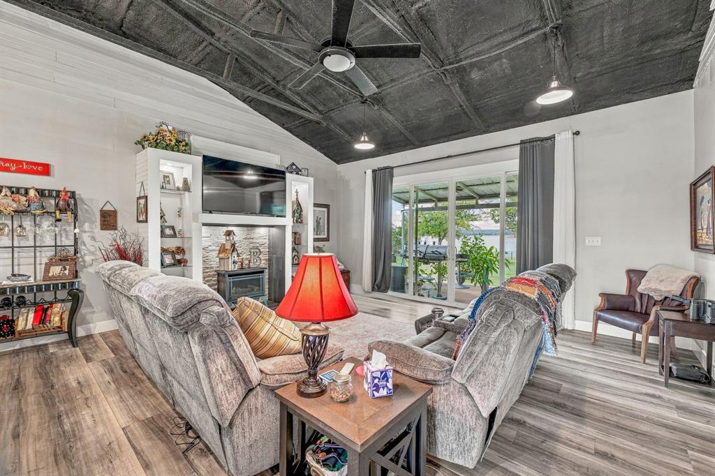 Living area featuring an exposed rafter ceiling, wood-finish vinyl flooring, floor-to-ceiling built-in shelving with an integrated propane fireplace, and sliding glass doors opening to covered back porch