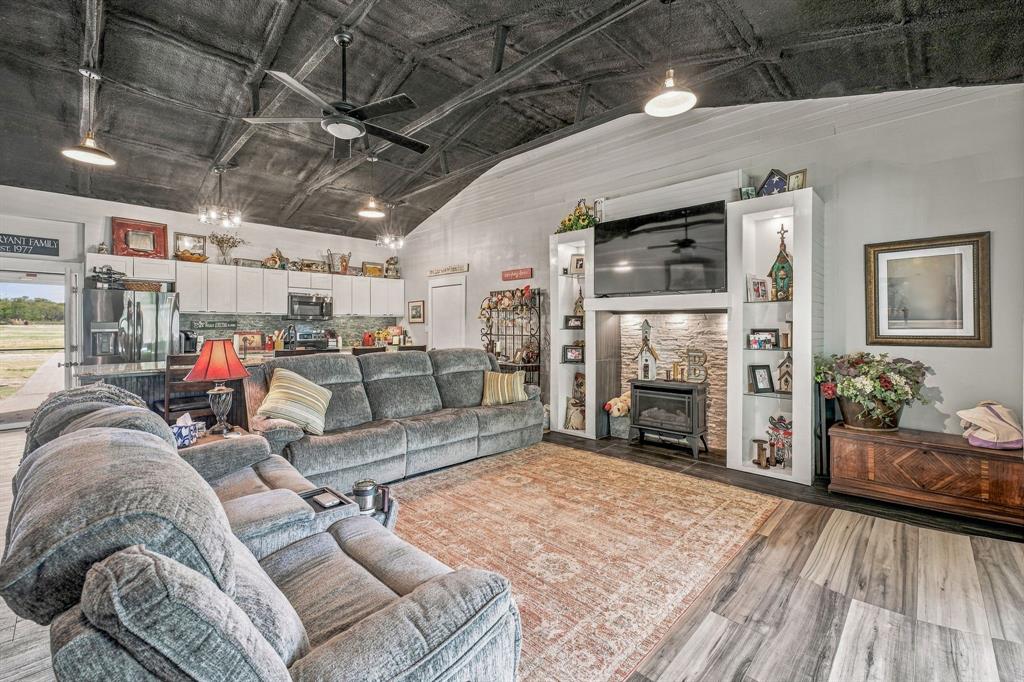 Vaulted ceiling with exposed structural elements, wood-finish vinyl flooring, built-in entertainment center with integrated shelving, stone-surround fireplace insert, and contemporary pendant lighting