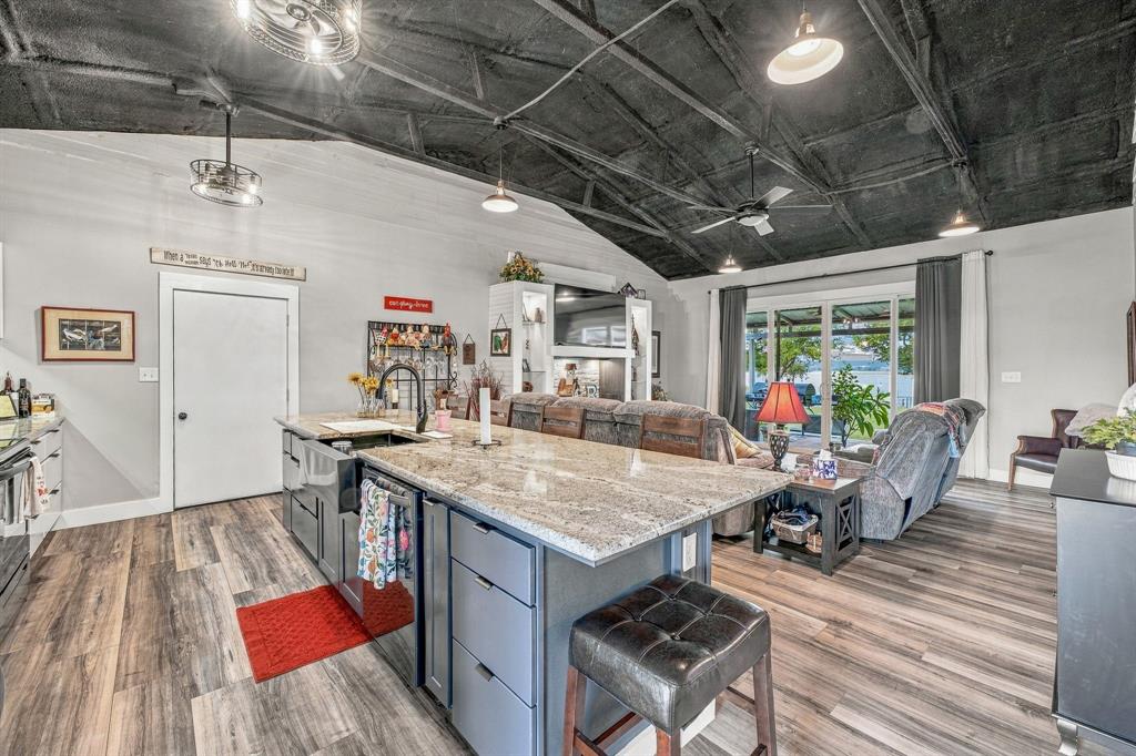 Vaulted ceiling with exposed structural beams, kitchen island with granite countertop, apron-front sink, wood-finish vinyl flooring, and integrated pendant and track lighting