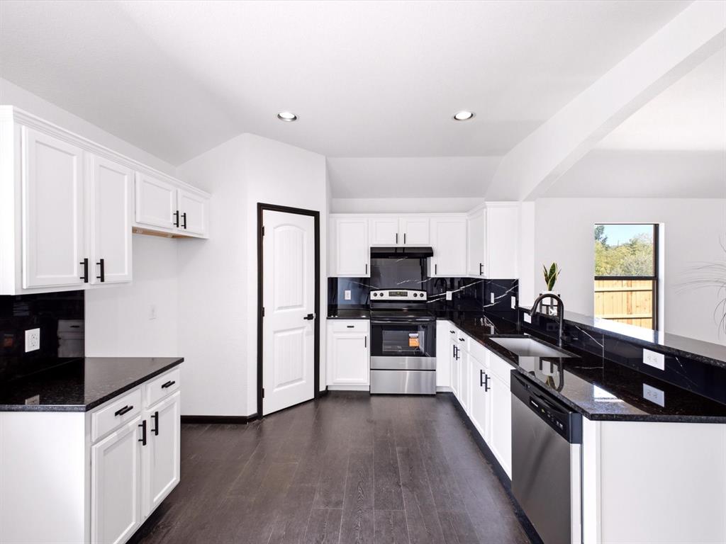 Kitchen featuring white shaker-style cabinetry, dark stone countertops, a full-height stone backsplash, stainless steel appliances, and dark-toned flooring