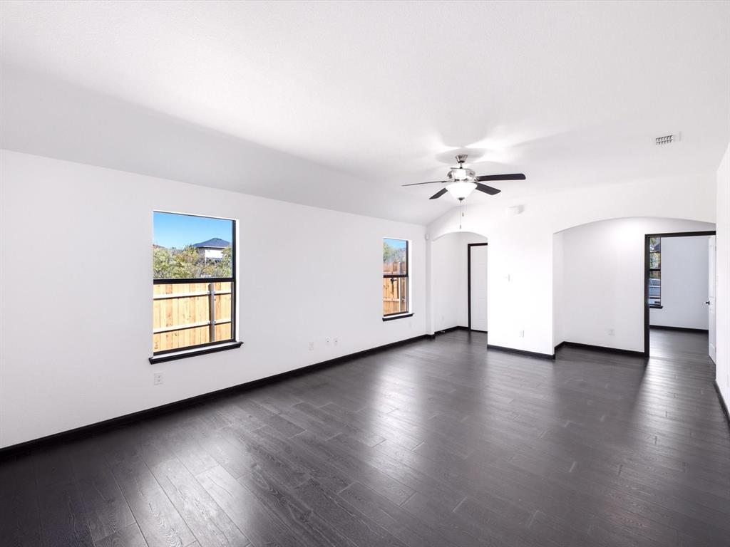 Interior space featuring dark wood-finish flooring, vaulted ceiling with a central light-integrated ceiling fan, two windows, and prominent arched architectural openings