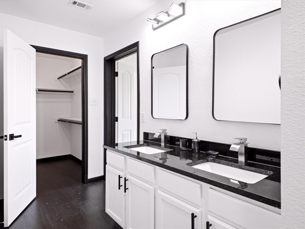Dual-sink vanity with dark stone countertop, undermount sinks, matte black cabinet hardware, framed mirrors, and dark wood-finish flooring