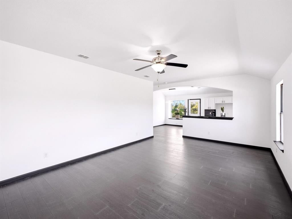 Vaulted ceilings, wood-finish flooring, recessed lighting, and a brushed nickel ceiling fan with integrated light fixture, featuring a partition wall with a pass-through opening