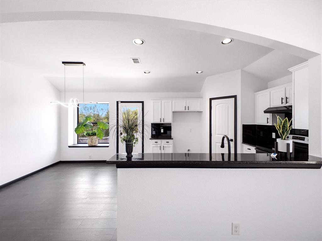 Kitchen featuring white shaker-style cabinetry, high-contrast black countertops, a deep-tone kitchen sink with a matte black faucet, recessed ceiling lighting, and large-format tile flooring