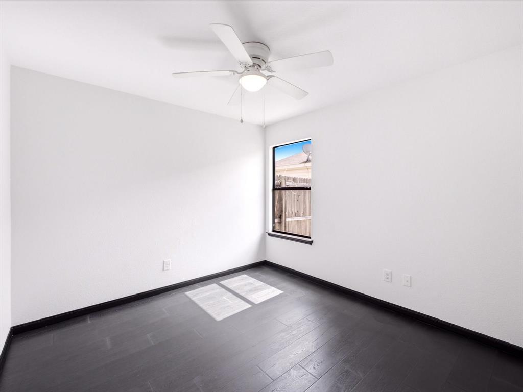 Room featuring dark wood-finish flooring, white walls, a ceiling fan with integrated light fixture, and a single-pane window